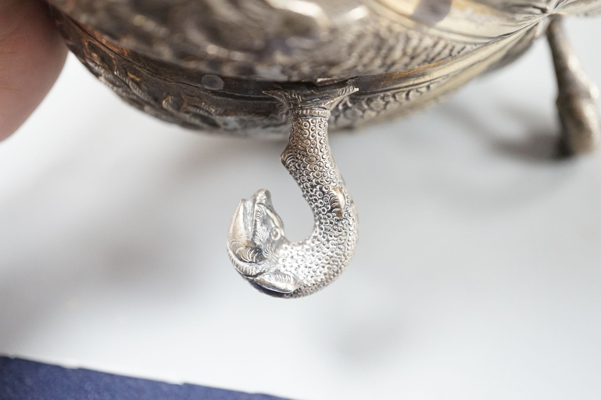 An Indian embossed white metal bowl, on three dolphin feet, diameter 13cm, 10oz.